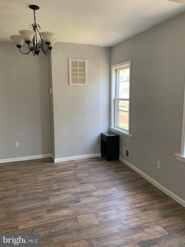 spare room featuring an inviting chandelier and dark hardwood / wood-style floors