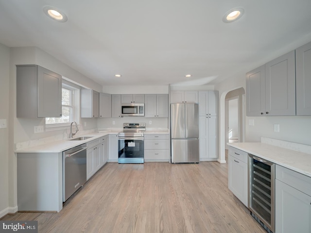 kitchen featuring sink, appliances with stainless steel finishes, gray cabinetry, wine cooler, and light wood-type flooring