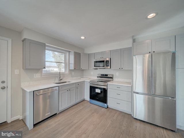 kitchen featuring appliances with stainless steel finishes, gray cabinets, sink, and light hardwood / wood-style flooring