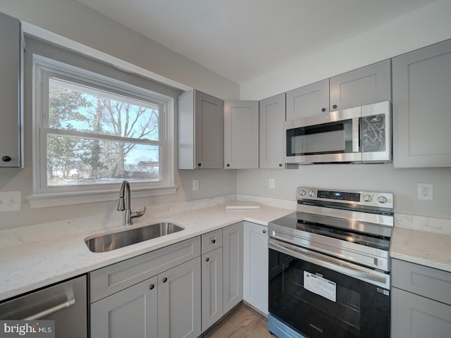 kitchen with gray cabinets, sink, light stone counters, stainless steel appliances, and light hardwood / wood-style flooring