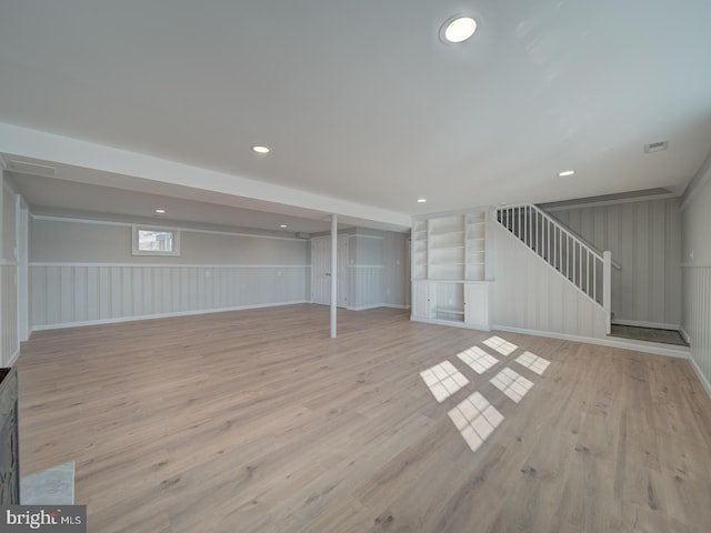 basement featuring light hardwood / wood-style flooring and built in shelves