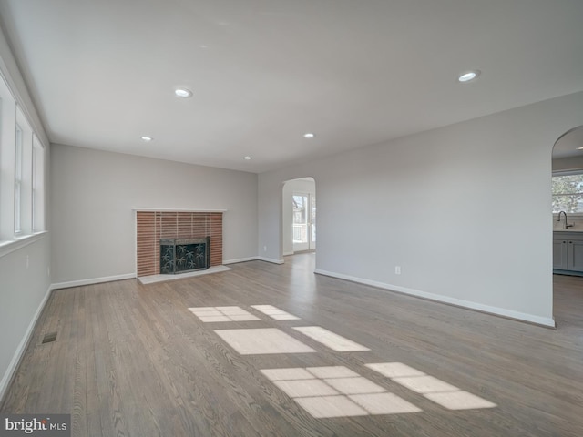 unfurnished living room featuring a healthy amount of sunlight, a fireplace, sink, and light wood-type flooring