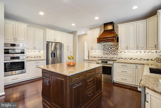 kitchen with dark brown cabinets, stainless steel appliances, light stone countertops, and custom exhaust hood