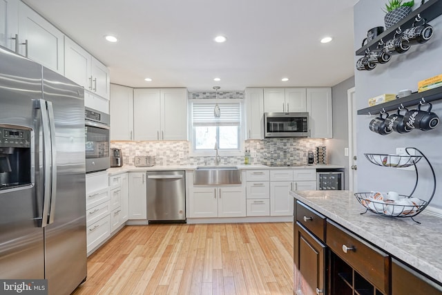 kitchen with appliances with stainless steel finishes, white cabinetry, light hardwood / wood-style floors, sink, and decorative backsplash