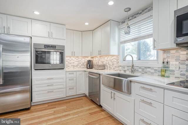 kitchen featuring pendant lighting, appliances with stainless steel finishes, white cabinetry, sink, and light wood-type flooring