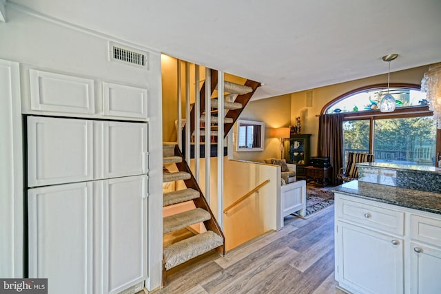 kitchen with pendant lighting, light hardwood / wood-style floors, dark stone counters, and white cabinets