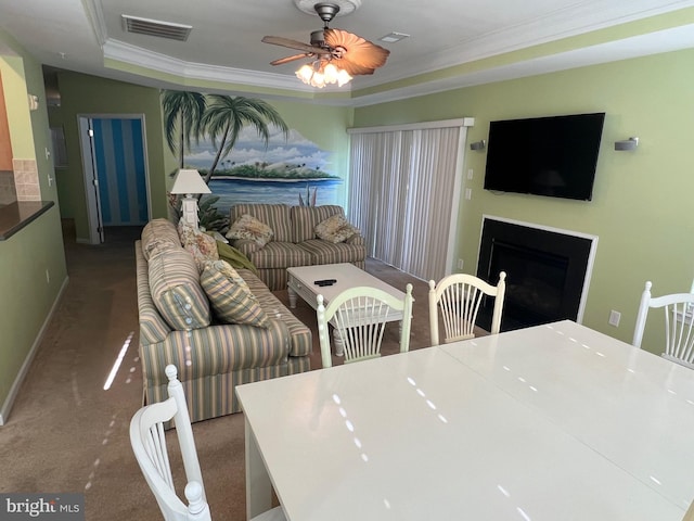 carpeted dining space with crown molding, ceiling fan, and a raised ceiling