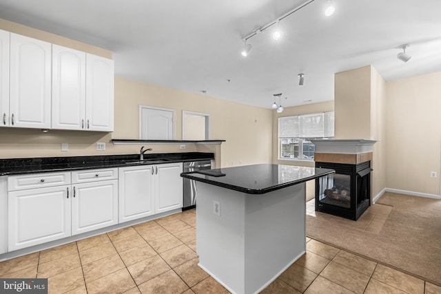 kitchen with light tile patterned flooring, white cabinetry, a center island, dishwasher, and a tiled fireplace