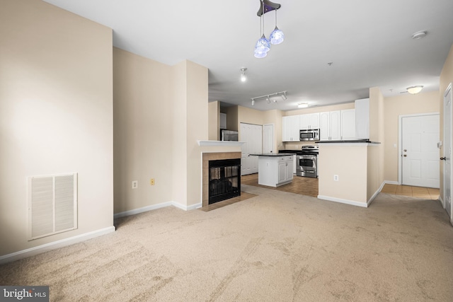 unfurnished living room featuring track lighting, a fireplace, and light colored carpet