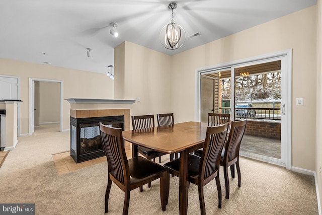 carpeted dining room featuring a tiled fireplace and a chandelier