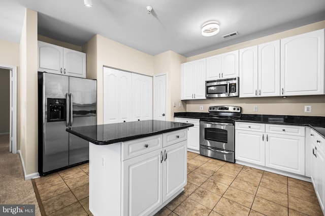 kitchen featuring light tile patterned flooring, dark stone counters, a kitchen island, stainless steel appliances, and white cabinets