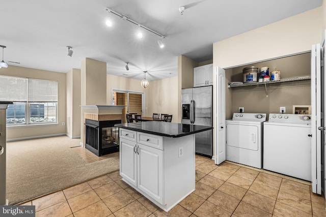 kitchen with washing machine and clothes dryer, a center island, stainless steel fridge with ice dispenser, light tile patterned floors, and white cabinets