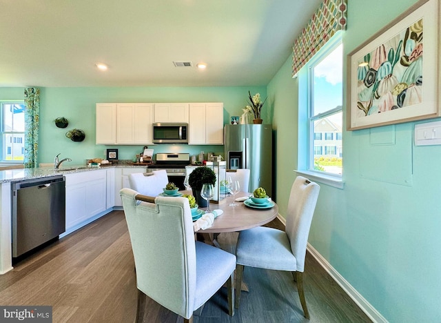 kitchen with appliances with stainless steel finishes, wood-type flooring, white cabinetry, sink, and light stone counters