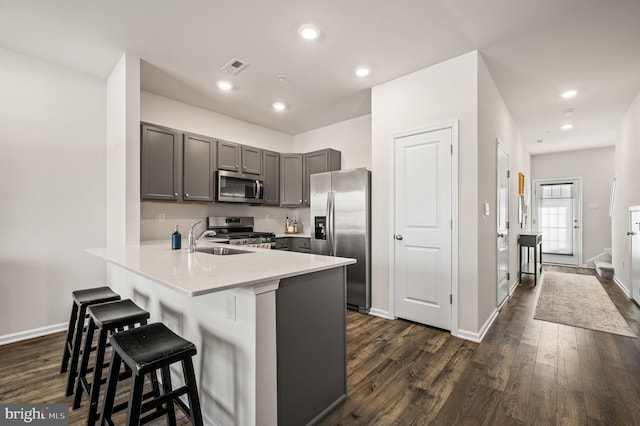 kitchen with a kitchen bar, dark hardwood / wood-style flooring, stainless steel appliances, sink, and kitchen peninsula