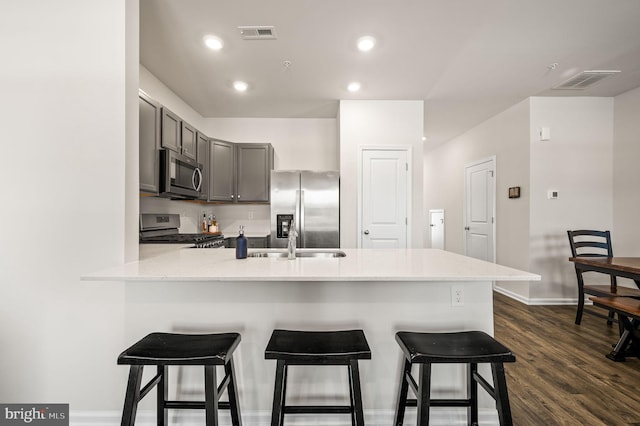 kitchen featuring dark hardwood / wood-style flooring, stainless steel appliances, kitchen peninsula, gray cabinetry, and a breakfast bar area