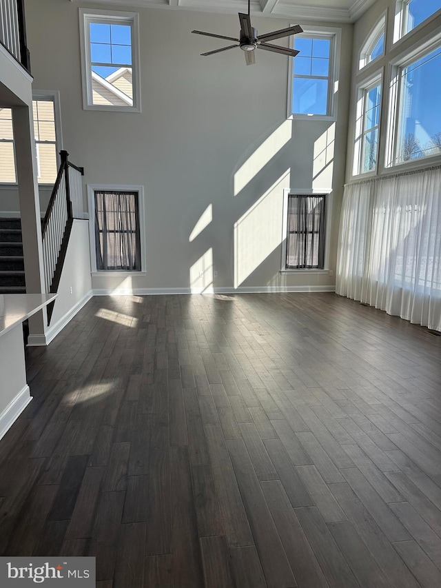 unfurnished living room with dark hardwood / wood-style floors, a towering ceiling, ceiling fan, and ornamental molding