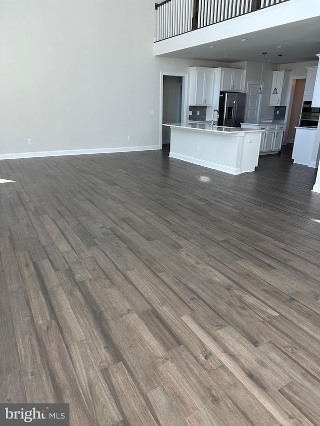 unfurnished living room featuring sink, a towering ceiling, and dark hardwood / wood-style flooring