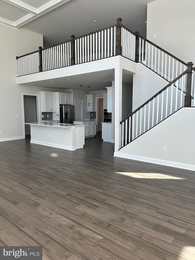 unfurnished living room with sink, dark hardwood / wood-style flooring, crown molding, and a towering ceiling