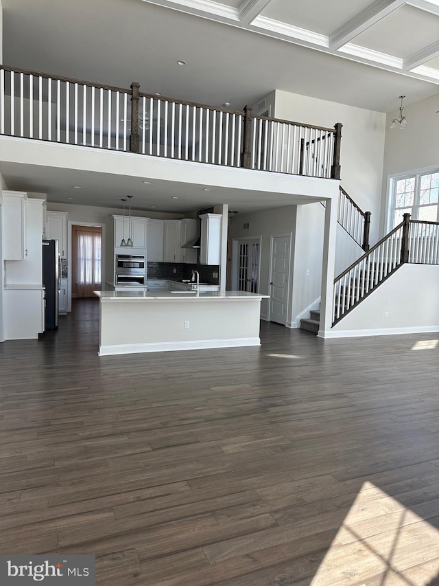 unfurnished living room with sink, dark wood-type flooring, a towering ceiling, beam ceiling, and coffered ceiling