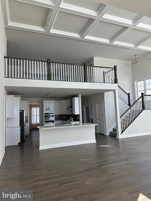 unfurnished living room with a towering ceiling, dark wood-type flooring, a notable chandelier, beam ceiling, and coffered ceiling