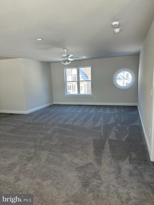 empty room featuring ceiling fan and dark colored carpet