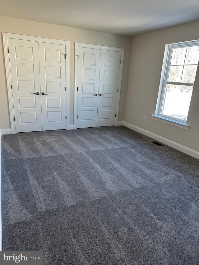 unfurnished bedroom featuring dark carpet and two closets