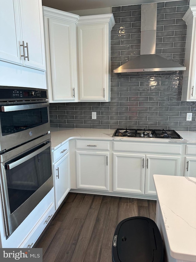 kitchen featuring wall chimney exhaust hood, white cabinets, tasteful backsplash, and appliances with stainless steel finishes