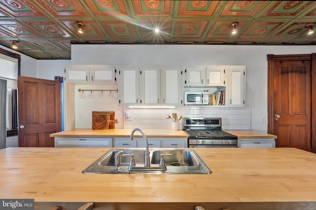 kitchen with stainless steel stove, wood counters, tasteful backsplash, sink, and white cabinets