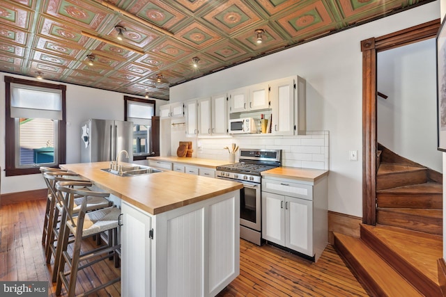 kitchen featuring sink, white cabinetry, wooden counters, stainless steel appliances, and a kitchen island with sink