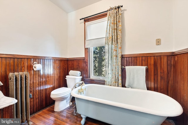 bathroom featuring radiator, hardwood / wood-style floors, wooden walls, a bathing tub, and toilet