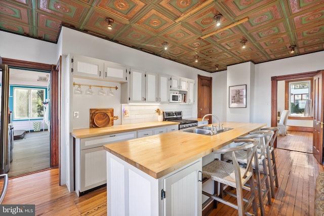 kitchen featuring butcher block counters, light hardwood / wood-style floors, an island with sink, stainless steel range oven, and white cabinets