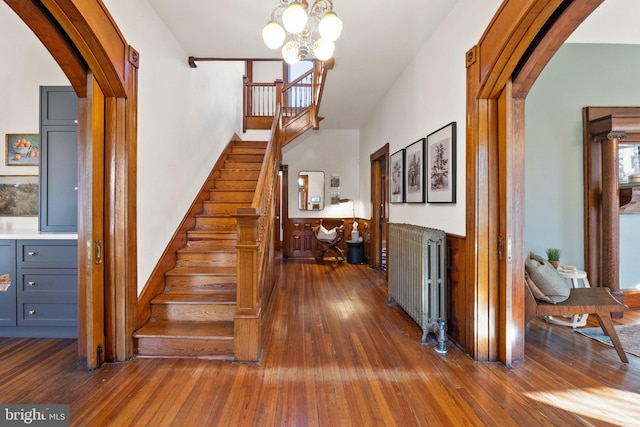 stairway with hardwood / wood-style flooring, radiator heating unit, and a notable chandelier