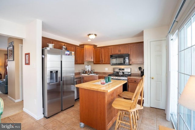 kitchen featuring a center island, wood counters, stainless steel appliances, light tile patterned flooring, and a breakfast bar