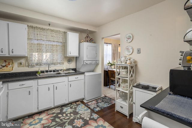 kitchen with stacked washing maching and dryer, dark wood-type flooring, white cabinetry, and sink