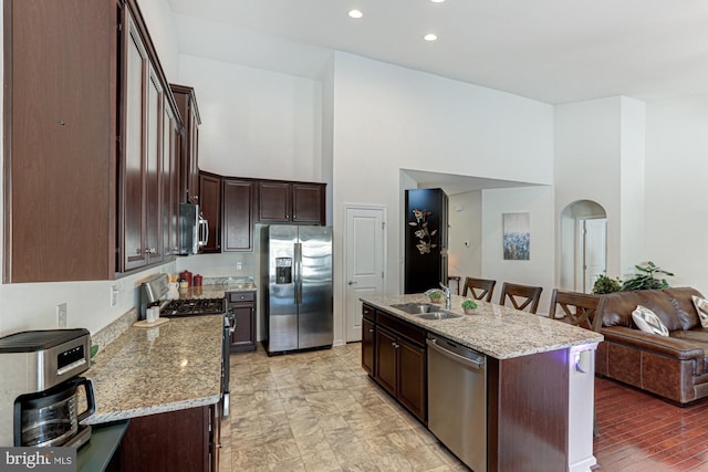 kitchen featuring dark brown cabinetry, stainless steel appliances, an island with sink, sink, and light stone counters