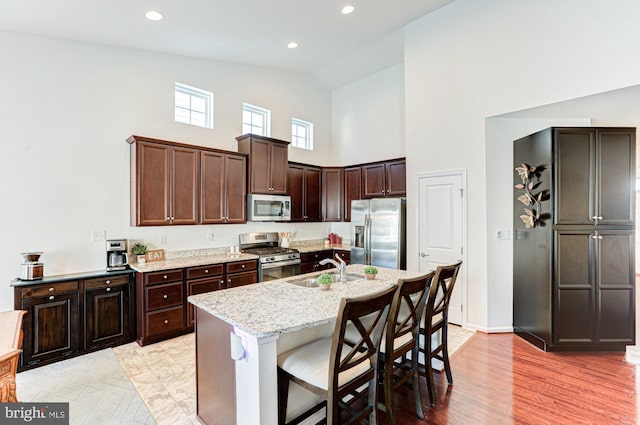 kitchen with appliances with stainless steel finishes, sink, light stone countertops, a kitchen bar, and a center island with sink