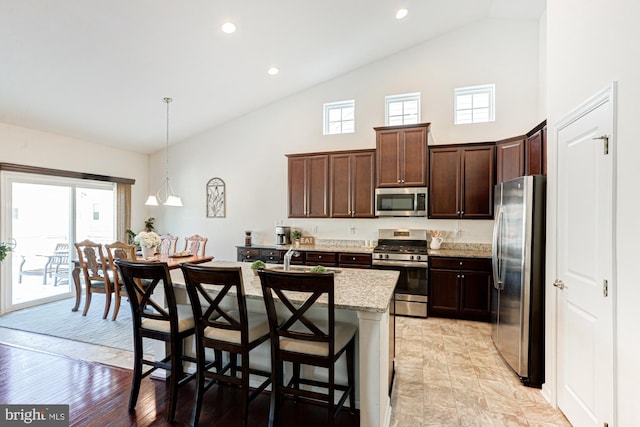 kitchen with light stone countertops, a kitchen island with sink, decorative light fixtures, a breakfast bar, and stainless steel appliances