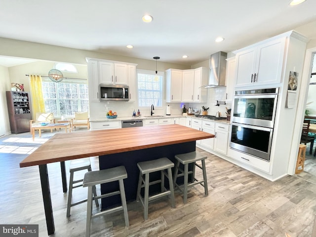 kitchen featuring tasteful backsplash, white cabinetry, sink, stainless steel appliances, and wall chimney exhaust hood