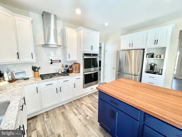 kitchen featuring blue cabinets, appliances with stainless steel finishes, wall chimney range hood, and white cabinets