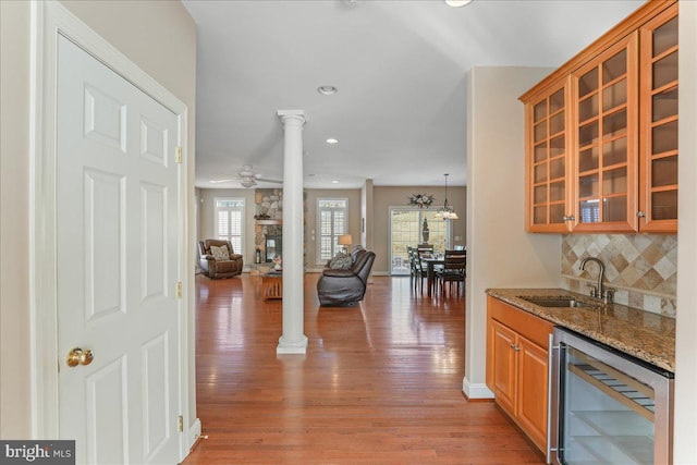 kitchen featuring ornate columns, tasteful backsplash, wine cooler, light stone countertops, and sink