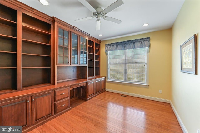 unfurnished office with light wood-type flooring, ceiling fan, and built in desk