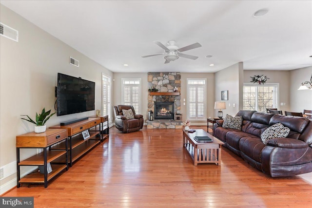 living room featuring light hardwood / wood-style floors, ceiling fan, and a stone fireplace