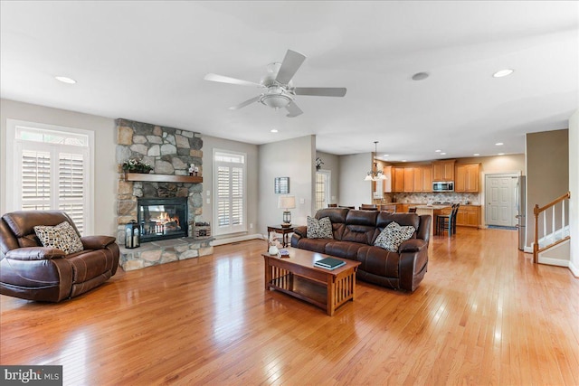 living room featuring ceiling fan, a wealth of natural light, light hardwood / wood-style flooring, and a stone fireplace