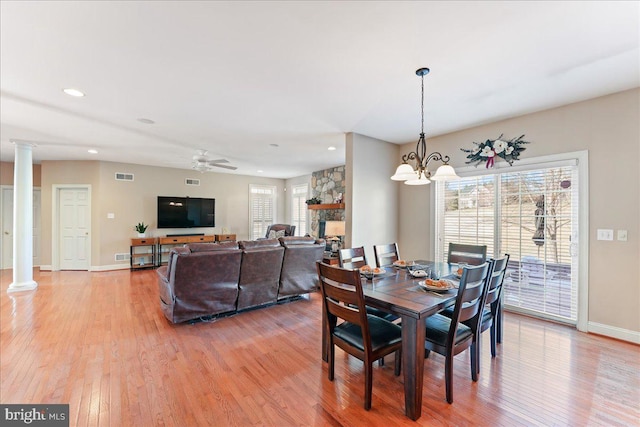 dining area with ceiling fan with notable chandelier, a fireplace, ornate columns, and light wood-type flooring