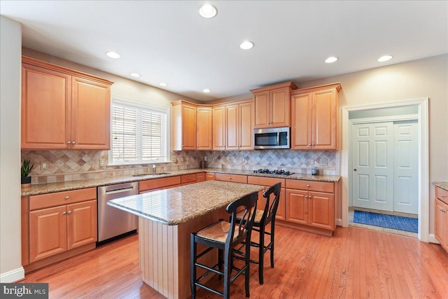 kitchen featuring a kitchen bar, stainless steel appliances, light wood-type flooring, light stone counters, and a center island