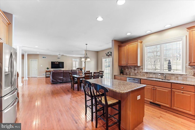 kitchen featuring a center island, sink, light stone countertops, appliances with stainless steel finishes, and decorative columns