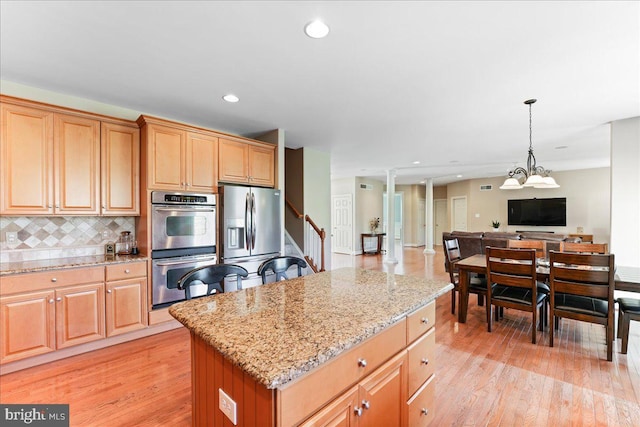 kitchen featuring light hardwood / wood-style floors, stainless steel appliances, backsplash, light stone counters, and a center island