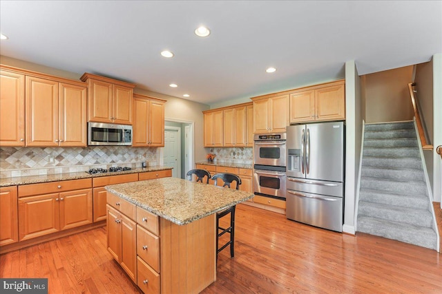 kitchen featuring light stone countertops, appliances with stainless steel finishes, a center island, tasteful backsplash, and a breakfast bar