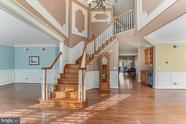 stairway featuring wood-type flooring, crown molding, a chandelier, and wine cooler