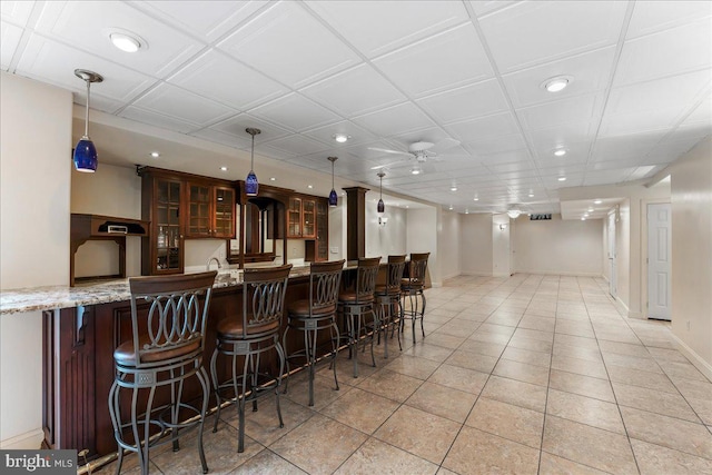 bar with light stone counters, hanging light fixtures, ceiling fan, and light tile patterned flooring